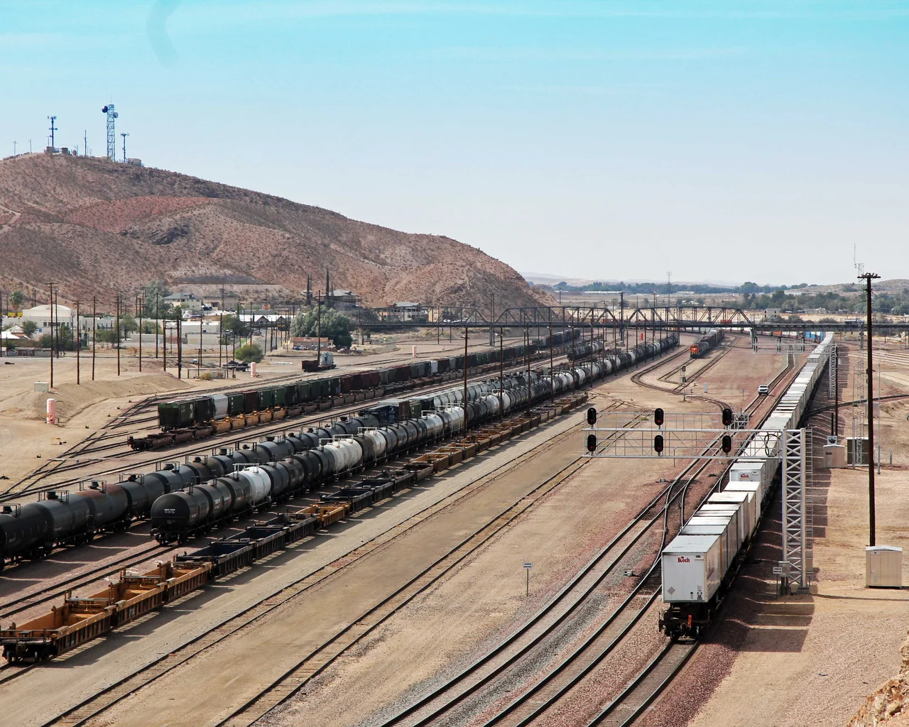 Barstow's BNSF classification yard in 2012: long strings of tank cars, boxcars and manifest freight on a desert track fan, a BNSF locomotive in the distance, the Barstow hill behind