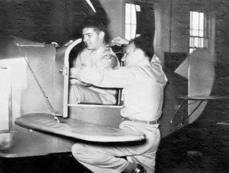 A cadet seated in a Link trainer flight simulator while an instructor leans in, 1944